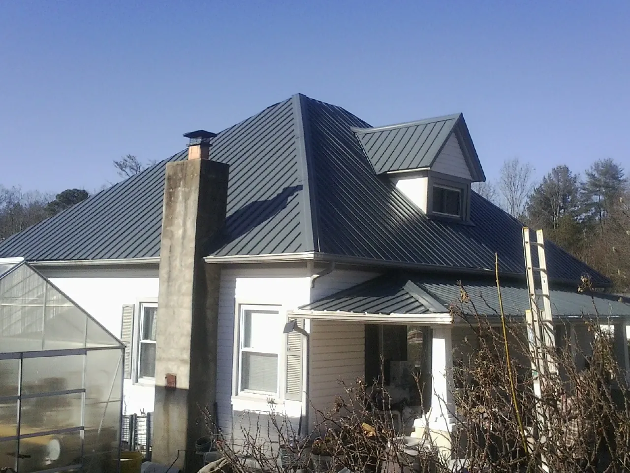 Dark blue standing seam metal roof on a white farmhouse with dormer — Slate & Tile Roof Repair by Roofing Brothers in Gould
