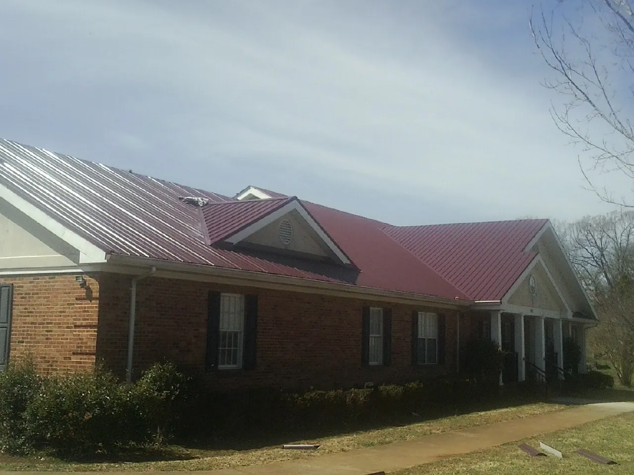 Red metal roof with gabled entries on a long brick building, from a Hail Damage Roof Repair job in Gould
