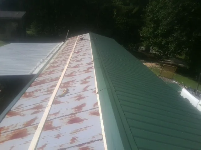 Old rusted panels beside newly installed green metal roofing — Wind Damage Roof Repair by Roofing Brothers in Gould
