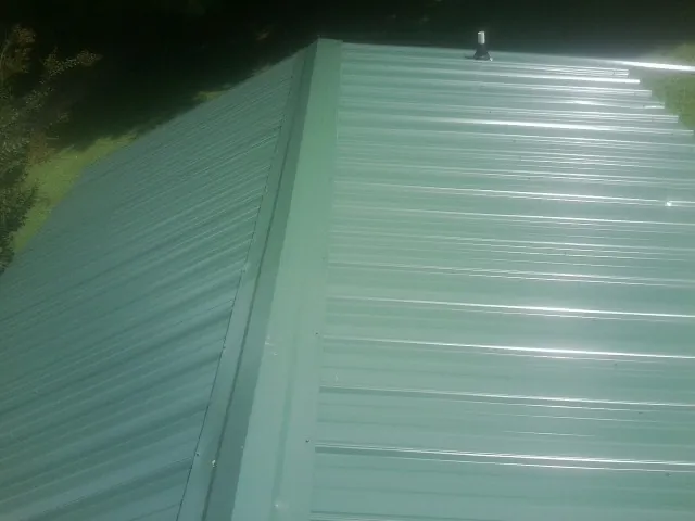 New green metal panels meeting at the ridge of a roof — Flat Roof Repair work by our crew in Gould