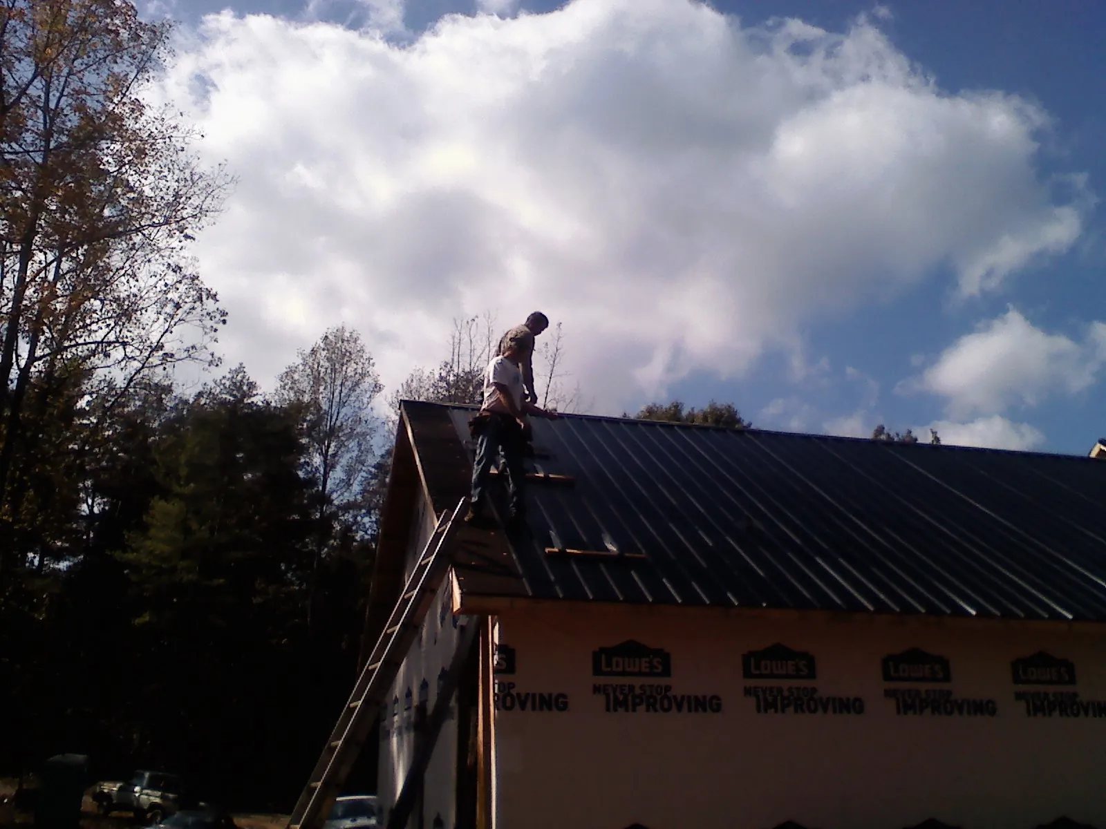Roofer fastening dark metal panels high against a cloudy sky, from a Roof Inspection job in Gould