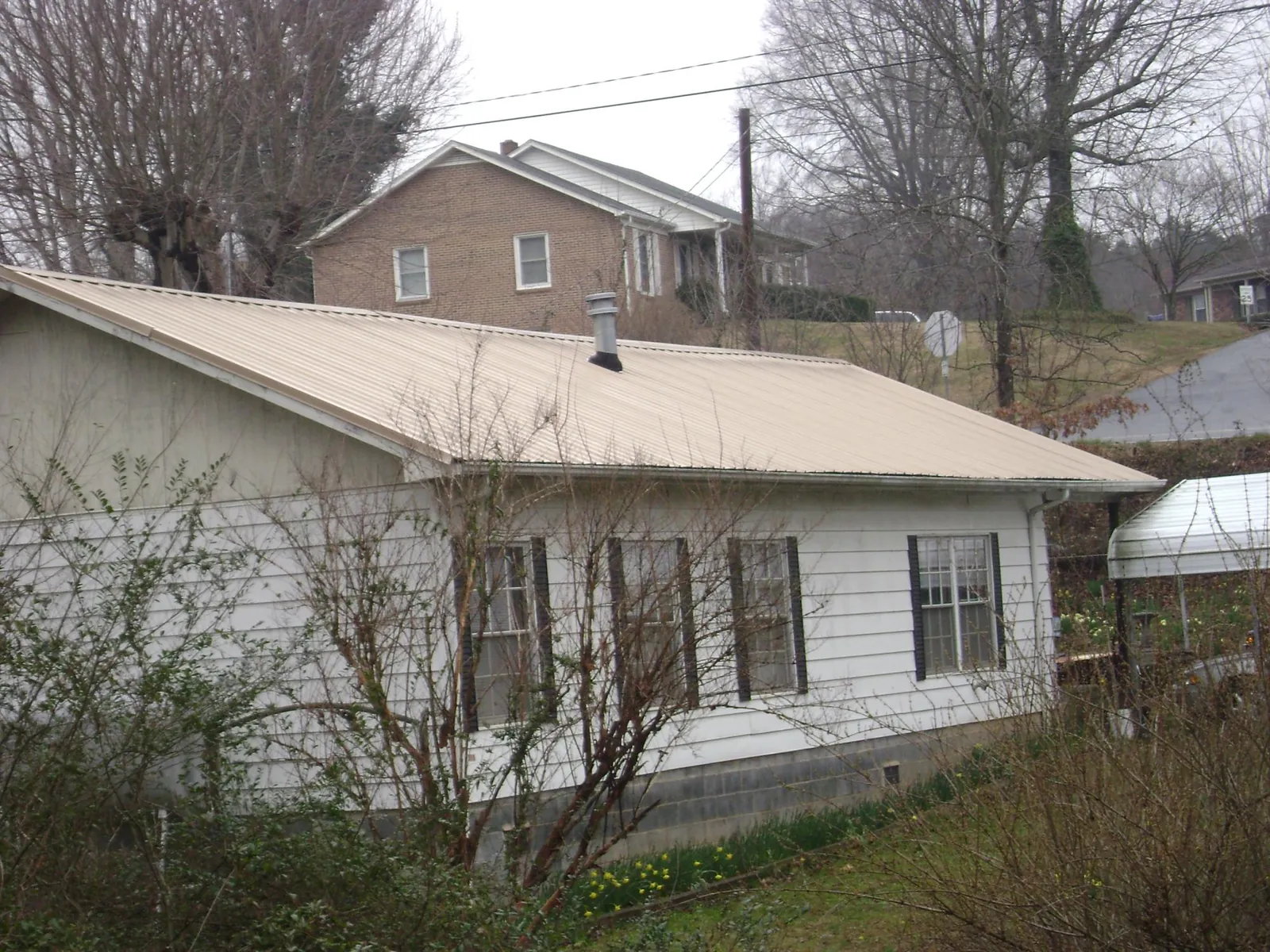 Tan metal roof on a white sided house set into a hillside — Commercial Roofing by Roofing Brothers in Gould