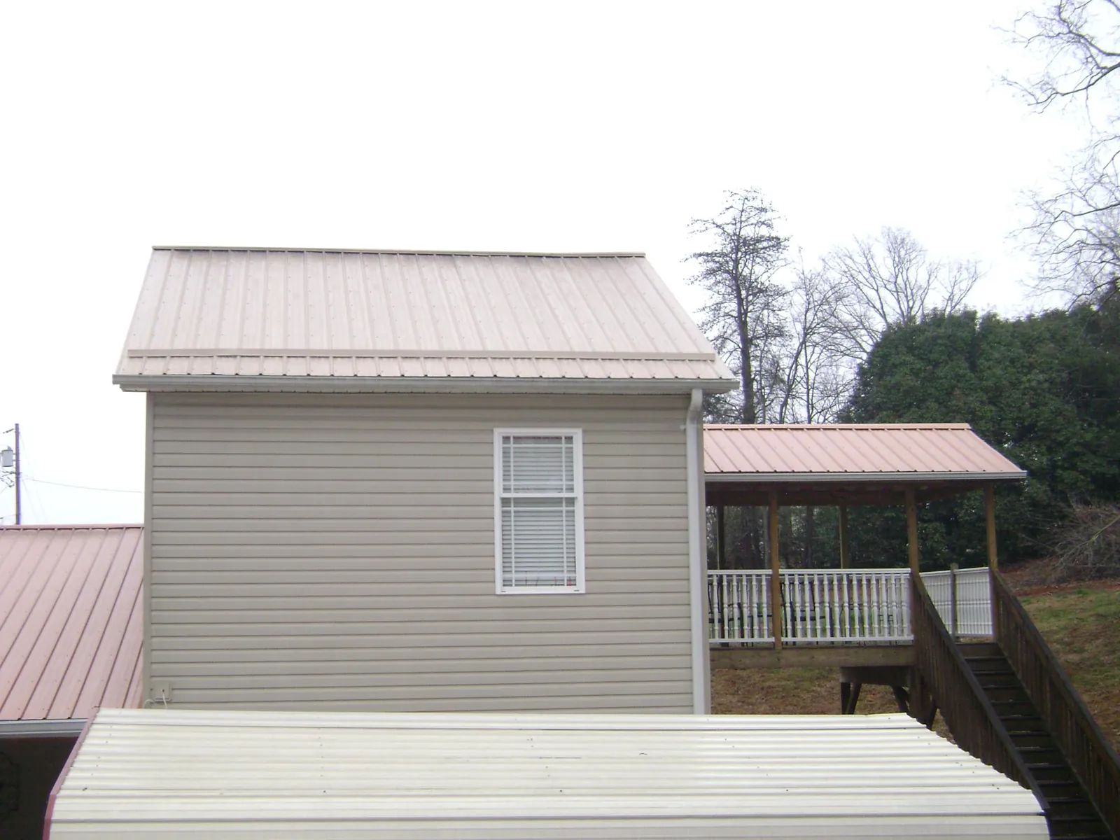 Tan metal roofs on a two story addition and attached porch, from a Roof Replacement job in Gould